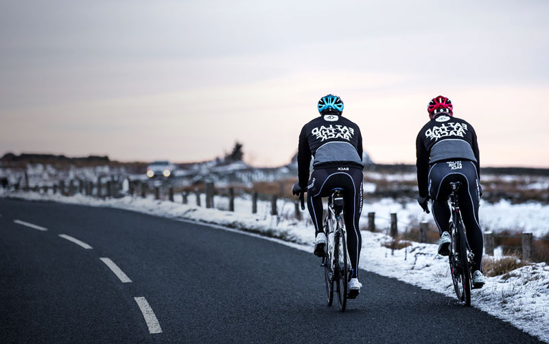 Två cyklister som cyklar på landsvägscyklar i ett snöigt landskap