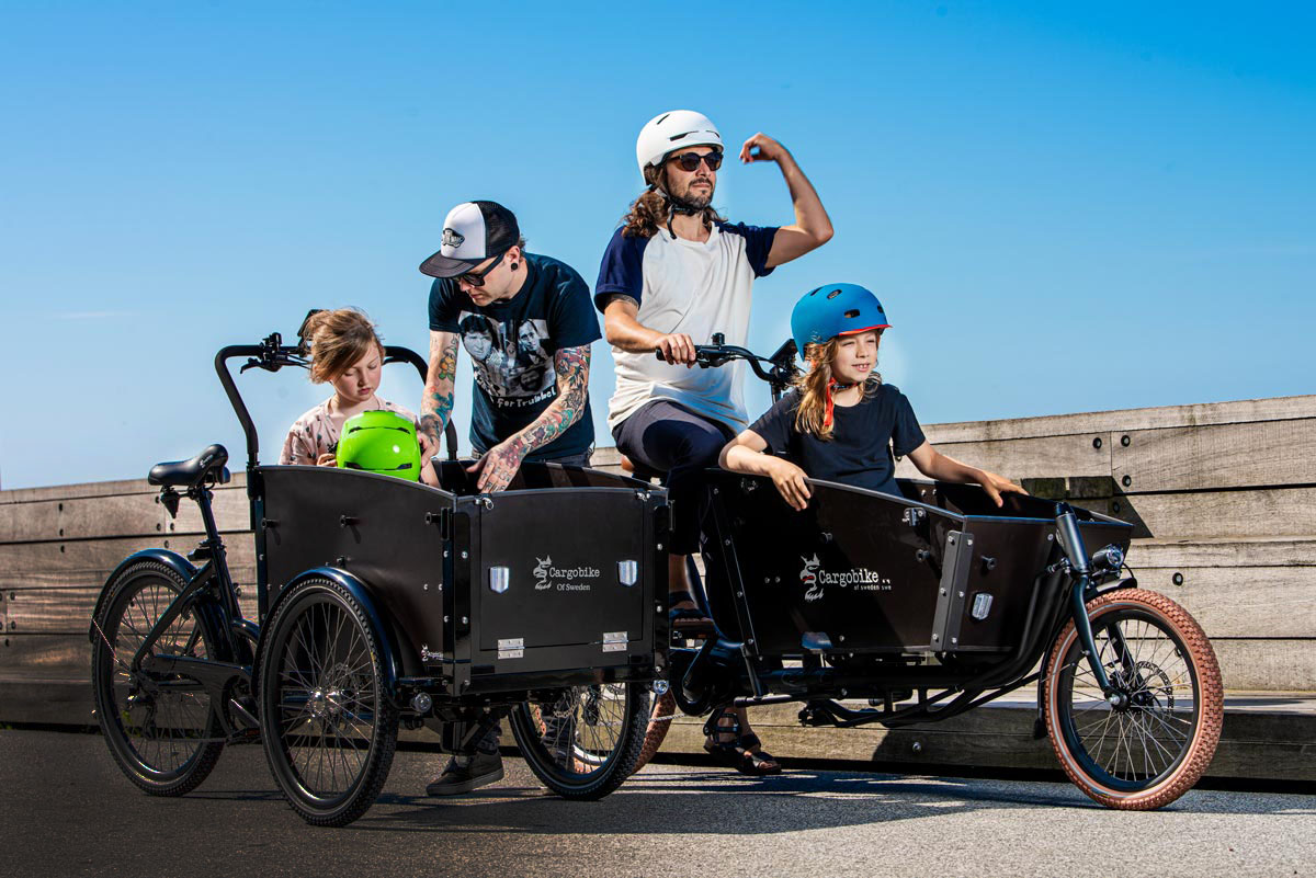Två föräldrar transporterar barn med varsin lastcykel